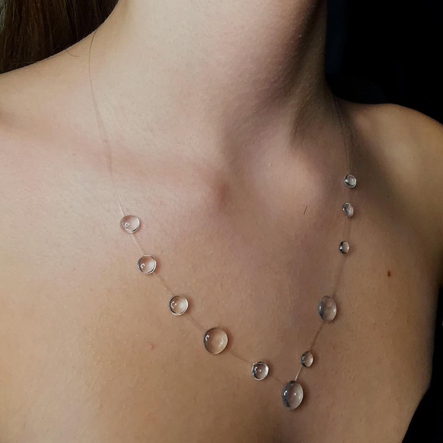 A delicate floating necklace featuring crystal-clear droplets, designed to mimic the elegance of raindrops suspended on an invisible strand. The lightweight and ethereal jewelry piece rests effortlessly on the wearer's collarbone, creating a natural and minimalist aesthetic. Perfect for a modern, nature-inspired look.