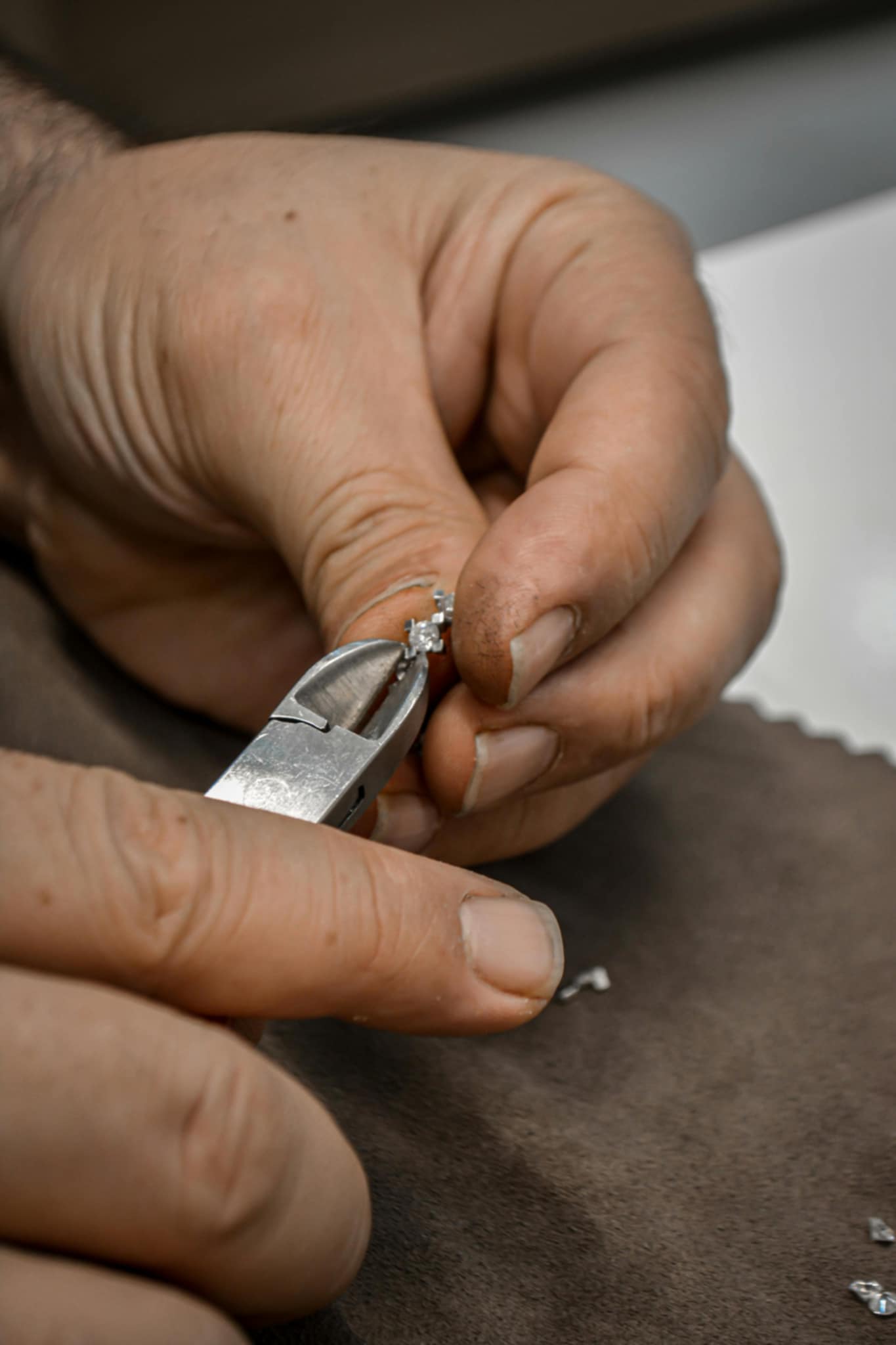 Close-up of a jeweler's hands carefully working on a small piece of jewelry using pliers. The detailed craftsmanship and fine work highlight the delicate nature of handmade jewelry creation.