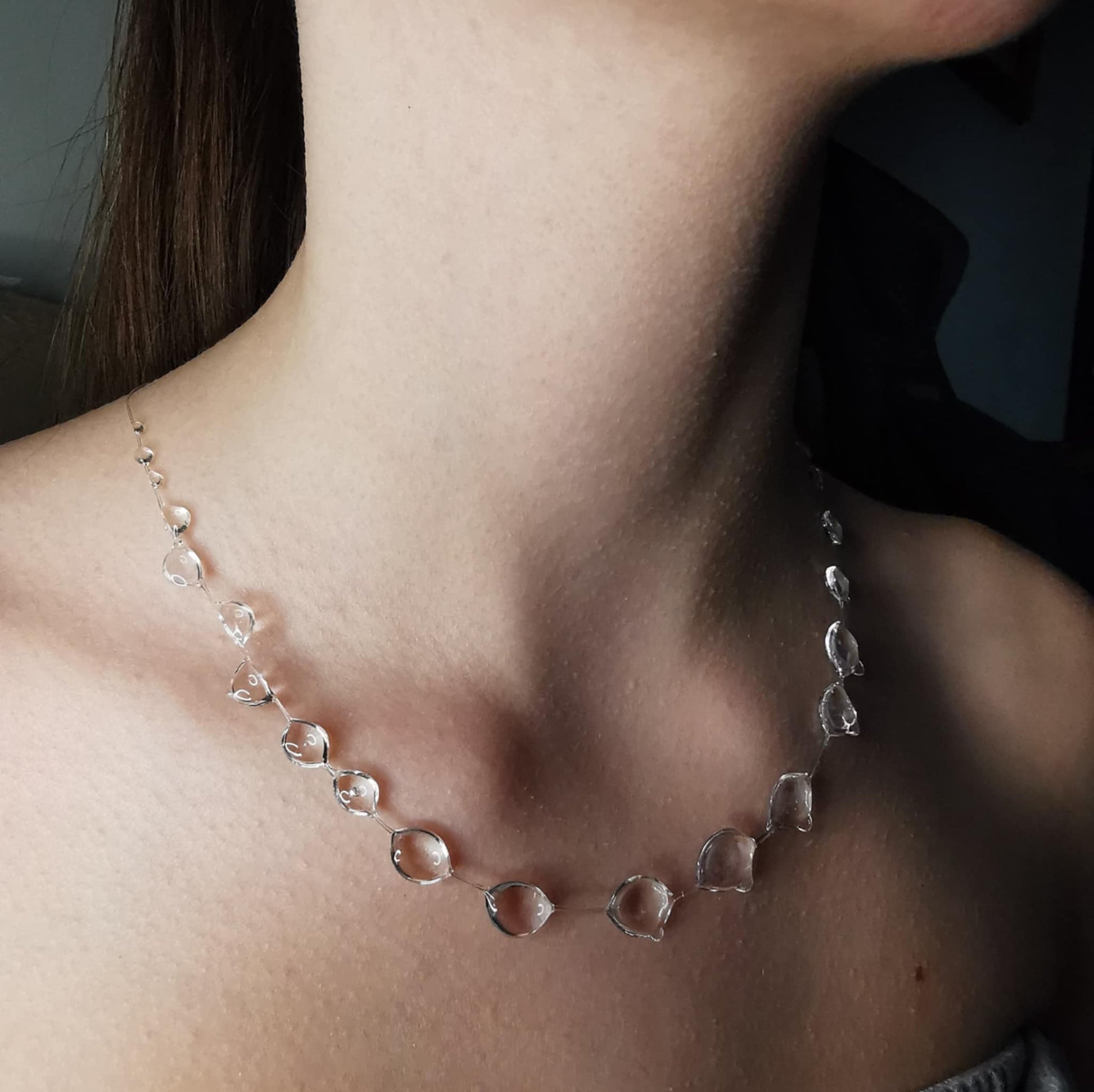 A delicate floating necklace featuring crystal-clear droplets, designed to mimic the elegance of raindrops suspended on an invisible strand. The lightweight and ethereal jewelry piece rests effortlessly on the wearer's collarbone, creating a natural and minimalist aesthetic. Perfect for a modern, nature-inspired look.